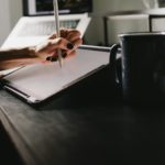 person writing on white paper on black table